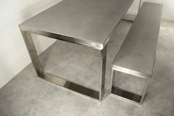 Mesa de comedor con banco en acero inox y tablero de cemento.