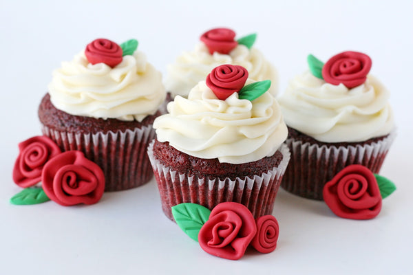 White cupcakes with red rose accents and marzipan leaves.
