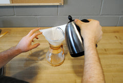 Filter inside Chemex brewer and someone pouring boiling water over top 