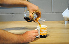 Person pouring the brewed coffee out of the Chemex into a coffee mug