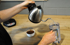 Person pouring boiling water from a kettle into a press pot
