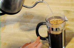 Someone pouring boiling water into the press pot with coffee grinds