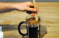 Someone sitrring the coffee and water in the press pot