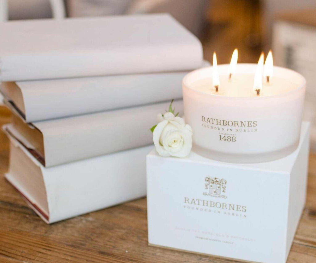 White scented candle next to pile of white books on wooden table