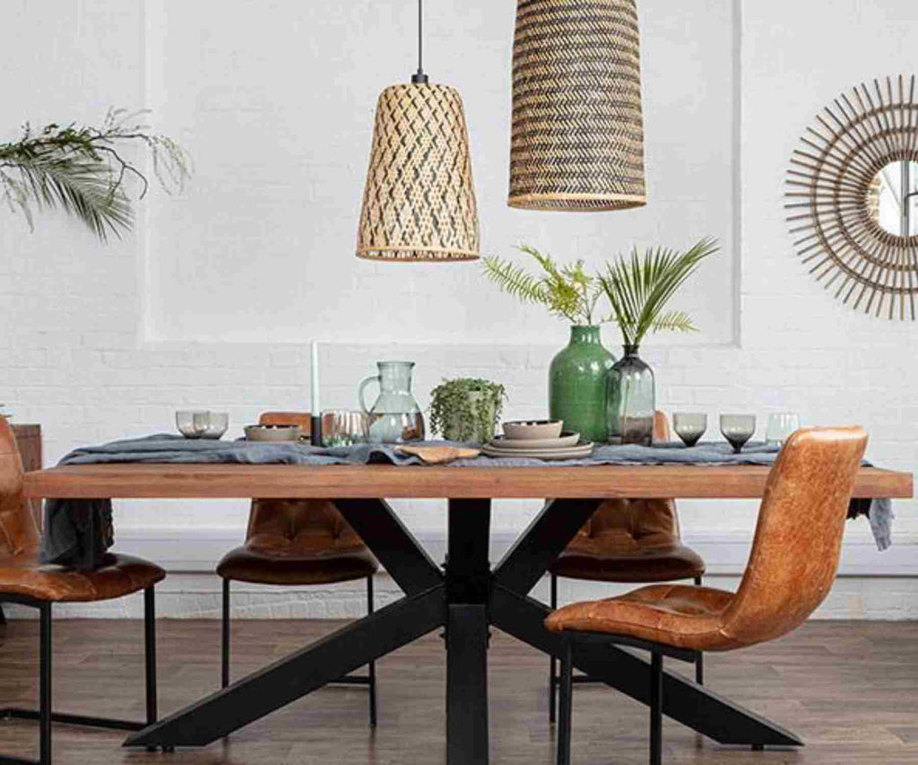 Tapered bamboo pendant lights over wooden table with black spider legs and brown faux leather chairs
