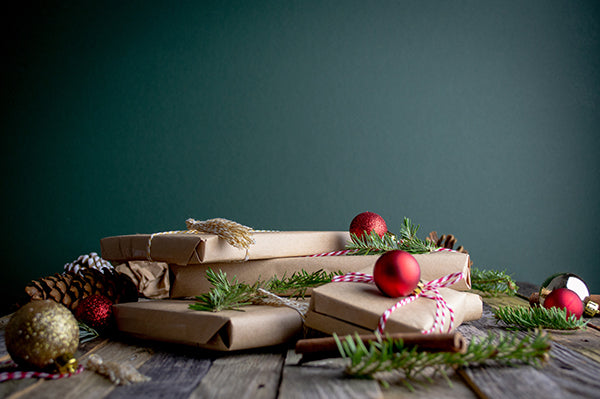 A wooden surface with Christmas decorations and gifts and a dark green backdrop
