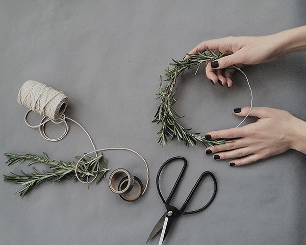 A person making a wreath out of greenery and thread