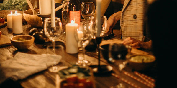 People huddled around a rustic dining table with lit candles, drinks and food