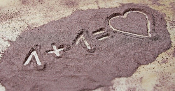 One plus one equals heart written in the sand
