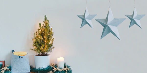 Small Christmas tree with fairy lights on a dark wooden mantelpiece with three hanging light blue stars