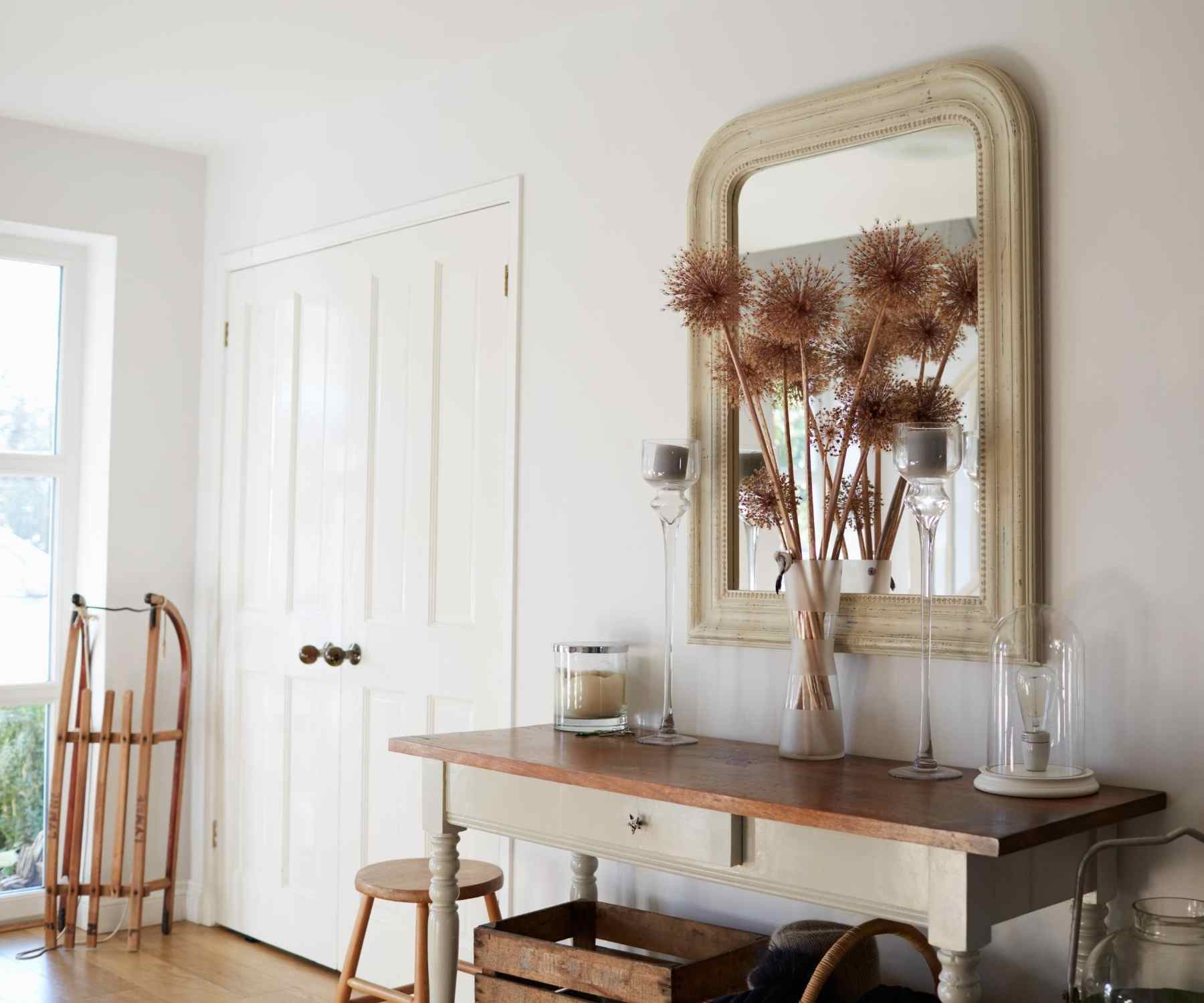 Bright hallway with wooden console table and mirror with dried flowers in vase