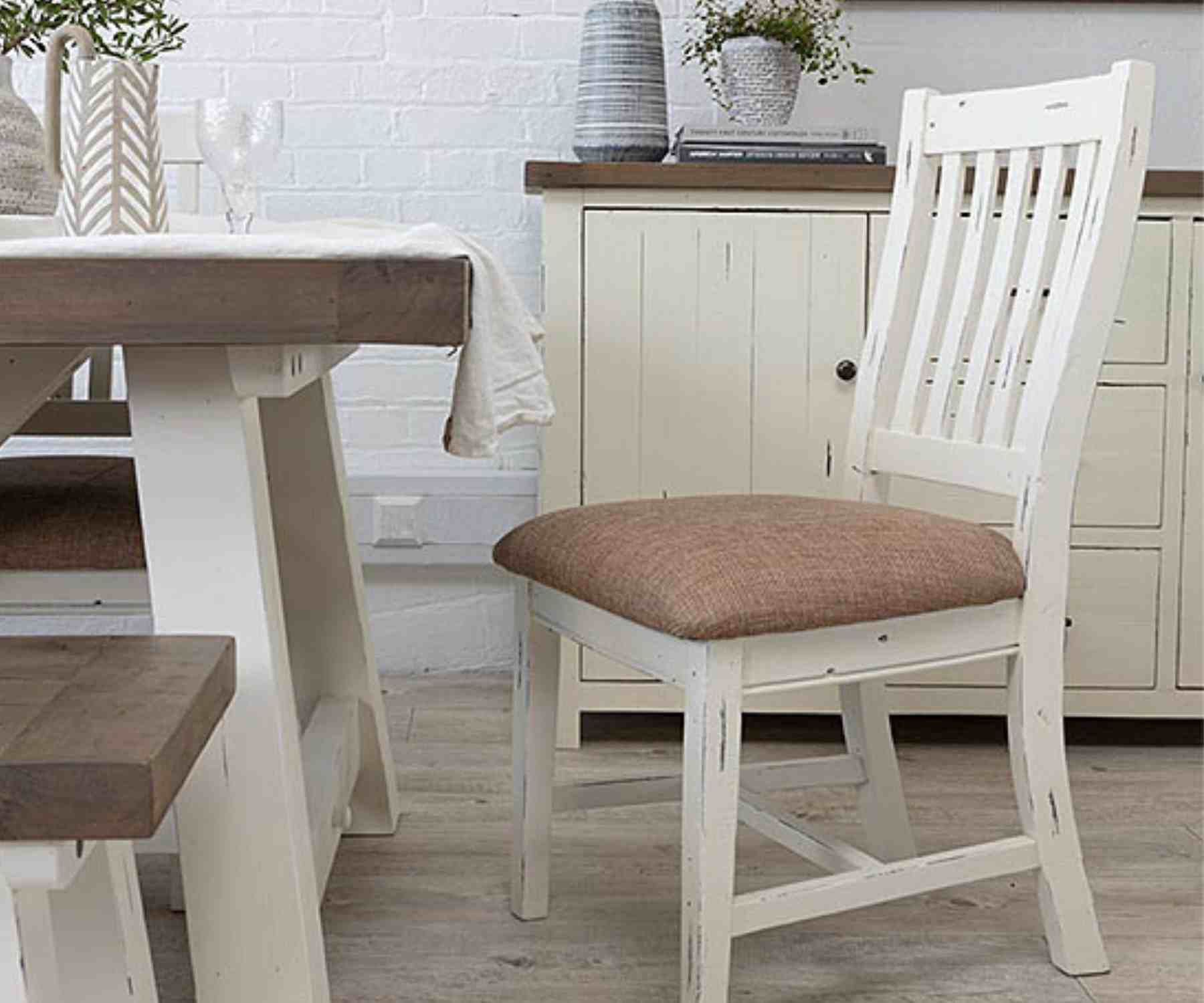 White wooden dining chair with beige padded seat next to white dining table