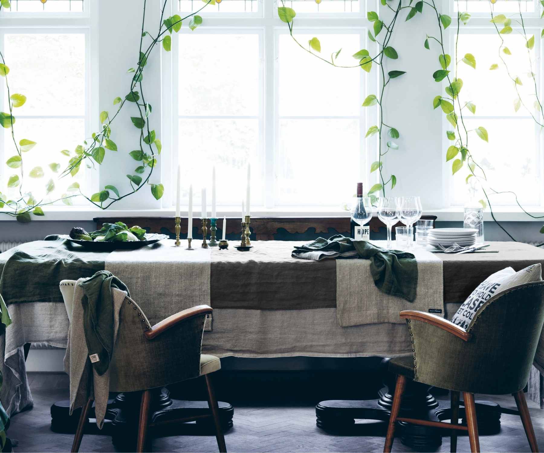 Dining table with layered linen tablecloths in front of large bright windows