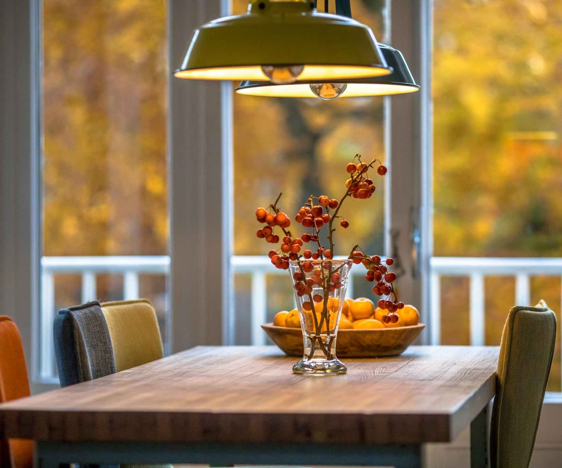 Wooden dining table with green pendant lighting and autumn berries