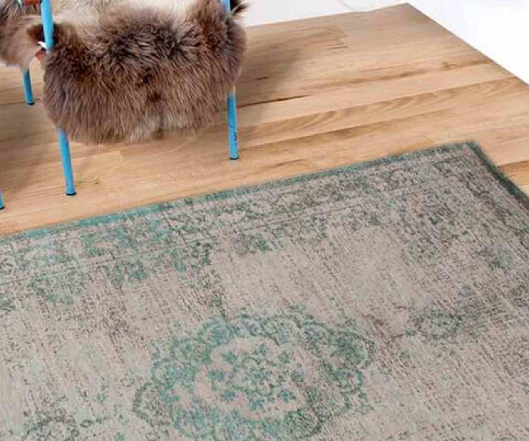 Faded green rug on wooden floor with metal chair and fur throw