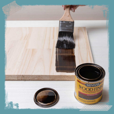 Paintbrush applying stain to wood. 