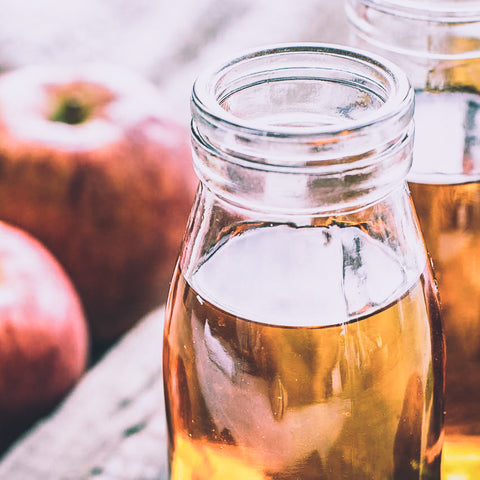 Clear bottle filled with apple cider vinegar on a table with apples nearby. 