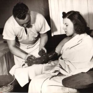 A man giving a woman a mud pack treatment on her arm. 