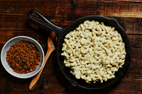 Bowl of toasted breadcrumbs next to a cast iron skillet filled with Howl Mac & Chef a vegan Mac and Cheese