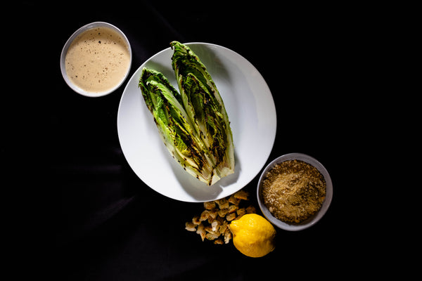 Recipe for grilled romaine lettuce, plant-based caesar dressing, parmesan crumble, croutons, lemon ready to be plated 
