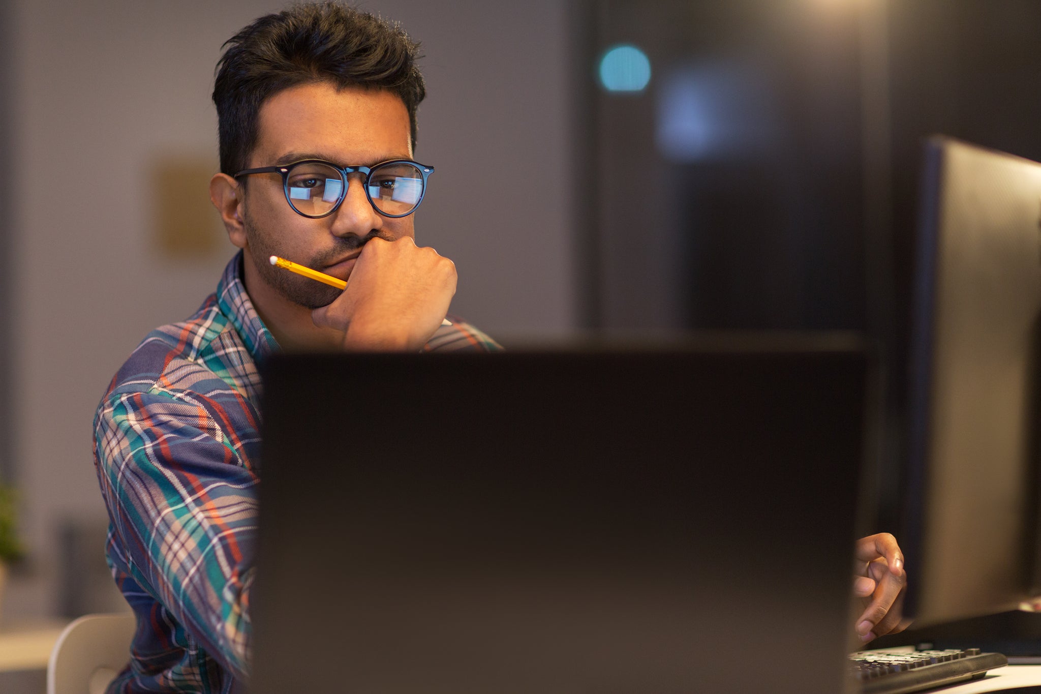 A man with eyeglasses staring at his laptop monitor.