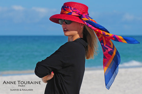 An ANNE TOURAINE Paris™ multicolor silk scarf tied around a red straw hat