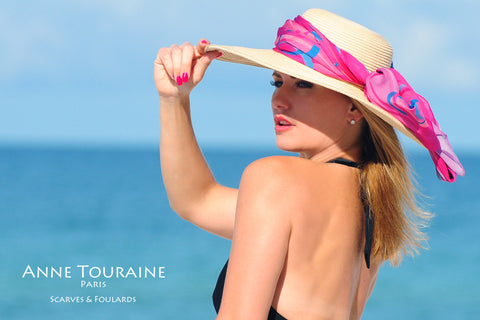 An ANNE TOURAINE Paris™ extra large chiffon silk scarf tied around a straw hat with a fluffy knot