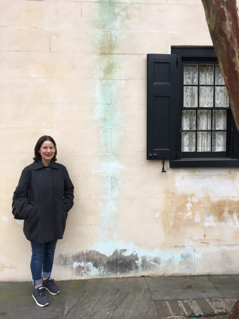 Barbara Sussberg, posing in front of an old house that is reminiscent of one of her textured paintings