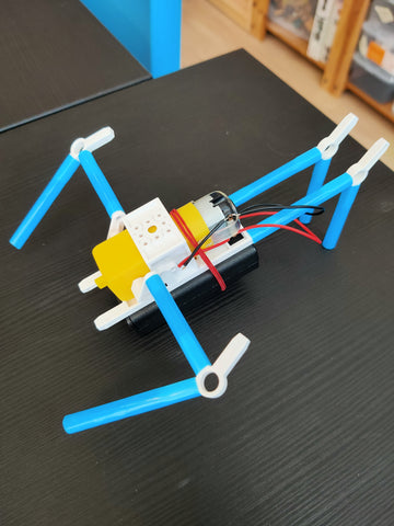 blue straw robot with white connectors and dc motor on black wooden table