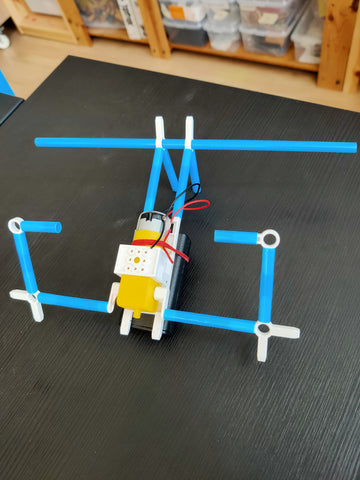 modified blue straw robot with white connectors and dc motor on black wooden table