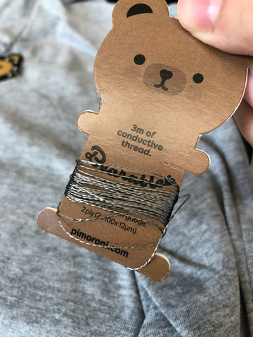 conductive thread coiled around a cute brown bear spool on a grey shirt background