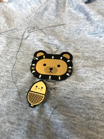assembled electronic bear badge and acorn sensor with conductive thread on grey shirt
