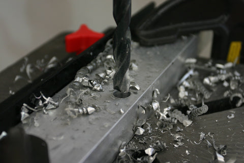 Full size drill bit in drill press drilling hole in aluminum bar stock to full diameter.