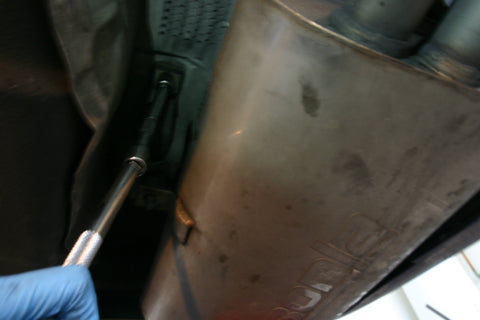 Muffler support bracket being unbolted using a socket and extension with a ratchet.