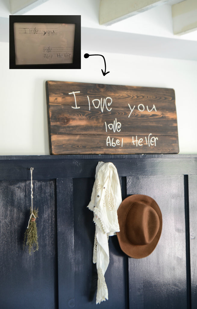Handwriting memory sign on wood above sweater and hat in mudroom "i love you"