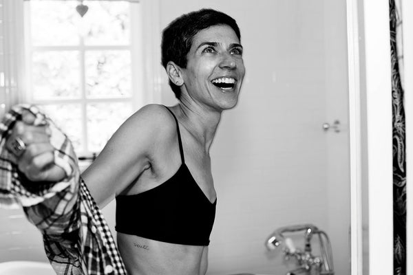 Samantha in the bathroom laughing with a flannel around her arms, just wearing a sports bra