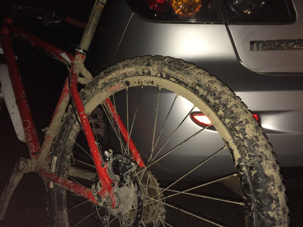 muddy mountain bike leaning against car