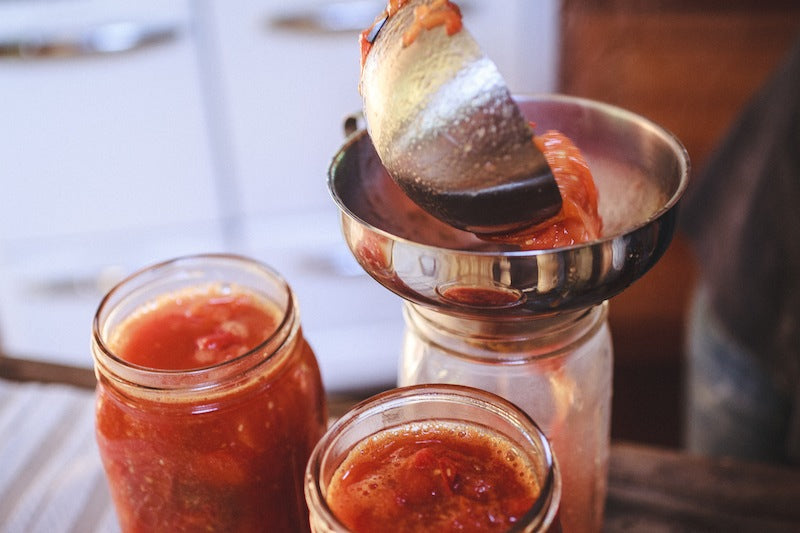 using a canning funnel to pack tomato sauce into canning jars using the hot pack method