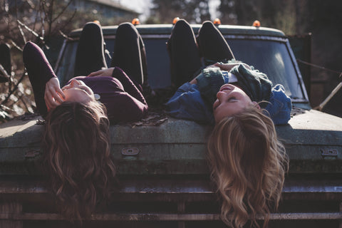 two friends smilingly happily together on the hood of a truck