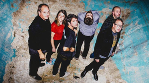 Six members of the band Cursive standing around at the bottom of a pool