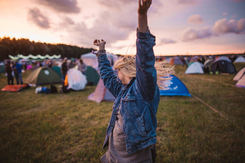 A young woman surrounded by tents and other festival gear.