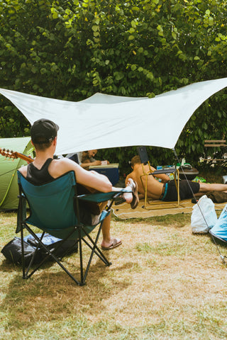 A group of young men relaxing under a shady canopy, playing guitar, taking photos, and using other items in our Festival Gear Guide.