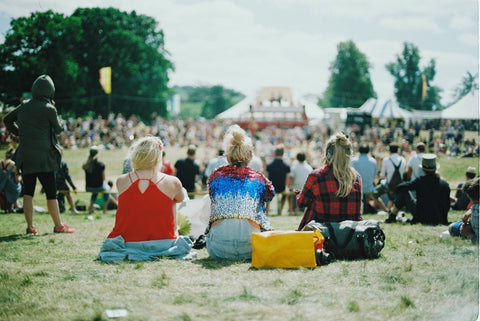 Three young women sitting on the music festival grounds and wearing stylish festival outfits.
