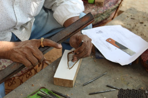 An artisan chipping away at a wood block as part of Passion Lilie's process for our clothes made in India.