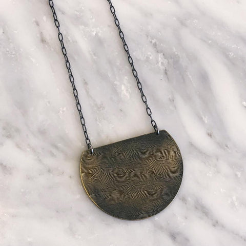 This Half Moon Necklace from Queens Metal is a flat, moon-shaped necklace in blackened gold with an intricate, wavy design.