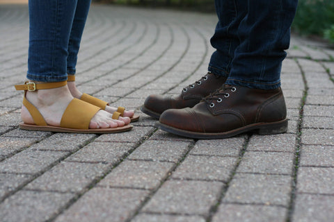 A fashionable yet comfortable pair of yellow women's sandals next to a sturdy and stylish pair of men's boots.