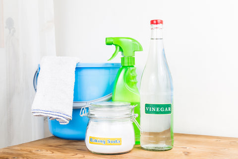 Picture of blue bucket with a cleaning towel, green spray bottle, baking soda, and a bottle of white vinegar.