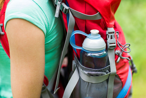 A plastic, reusable water bottle sits in a backpack pocket of a woman hiking