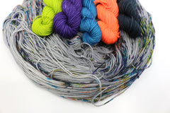 5 mini skeins (lime green, purple, blue, coral, and greeny-grey) sit atop a light grey skein speckled with those same colours