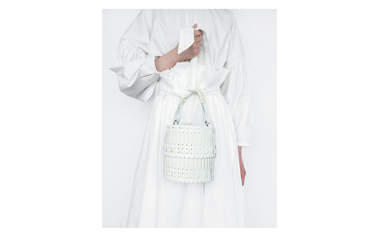 Image is a close-up crop of a White top and skirt by Shaina Mote with a hand holding a White leather bag by Hatori.